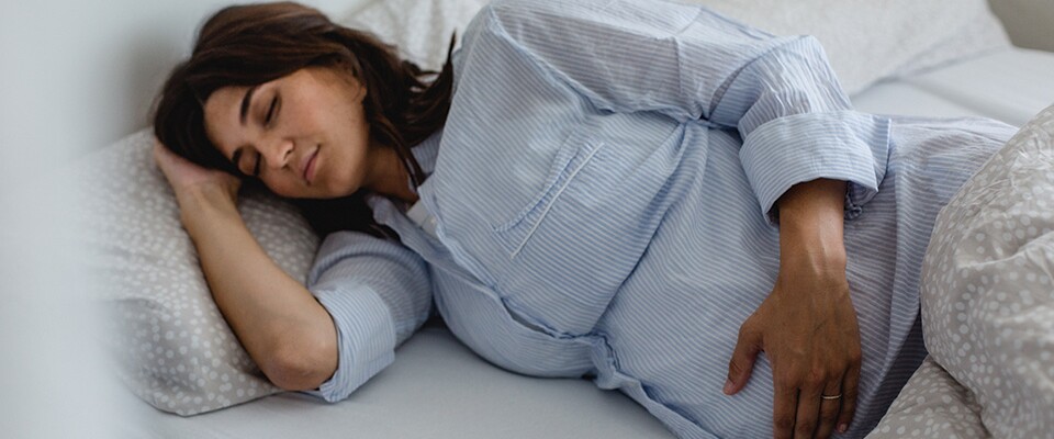 Schwangere Frau liegt seitlich schlafend im Bett